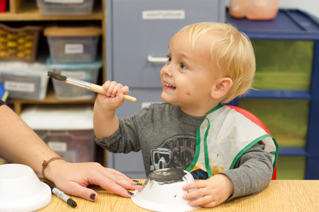 smiling little boy holding paint brush at a Preschool & Daycare Serving Carmel, Indiana