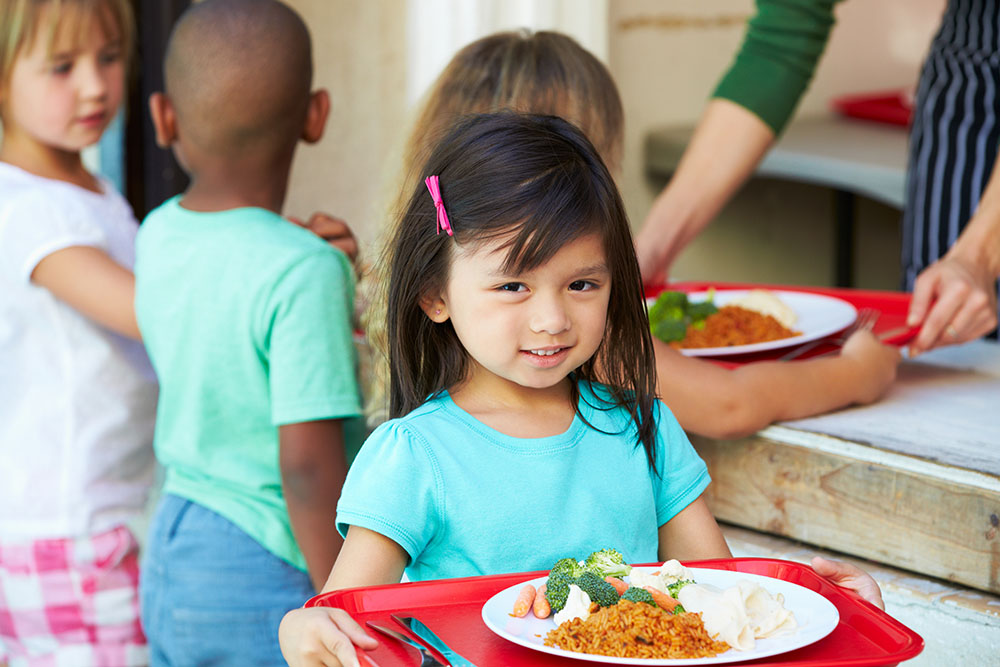 Elementary Pupils Collecting Healthy Lunch In Cafeteria at a Preschool & Daycare Serving Carmel, Indiana